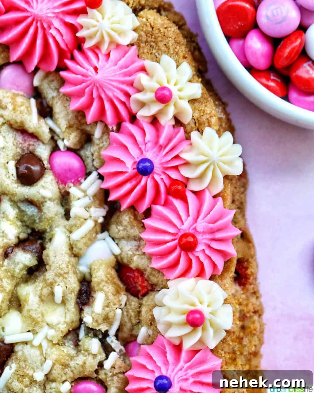 A heart-shaped Valentine's Day cookie cake with pink and white vanilla frosting and red, white, and pink M & M decorations.