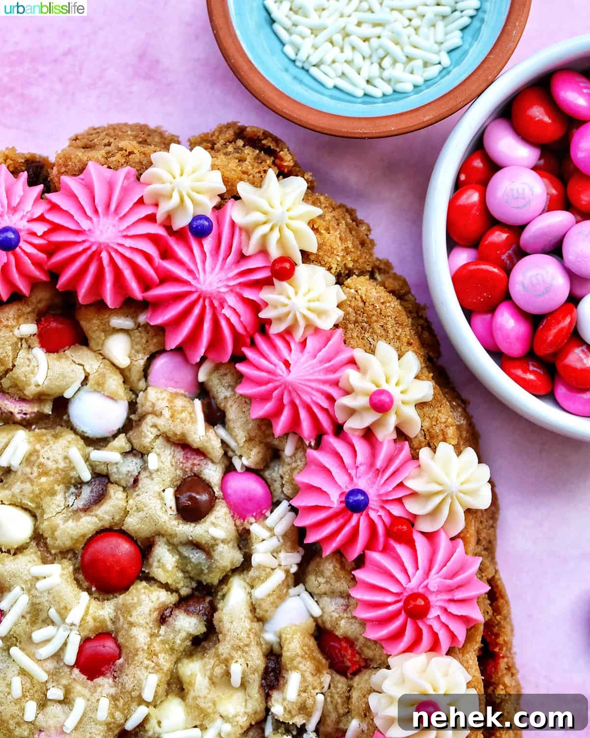 A heart-shaped Valentine's Day cookie cake with pink and white vanilla frosting and red, white, and pink M & M decorations.