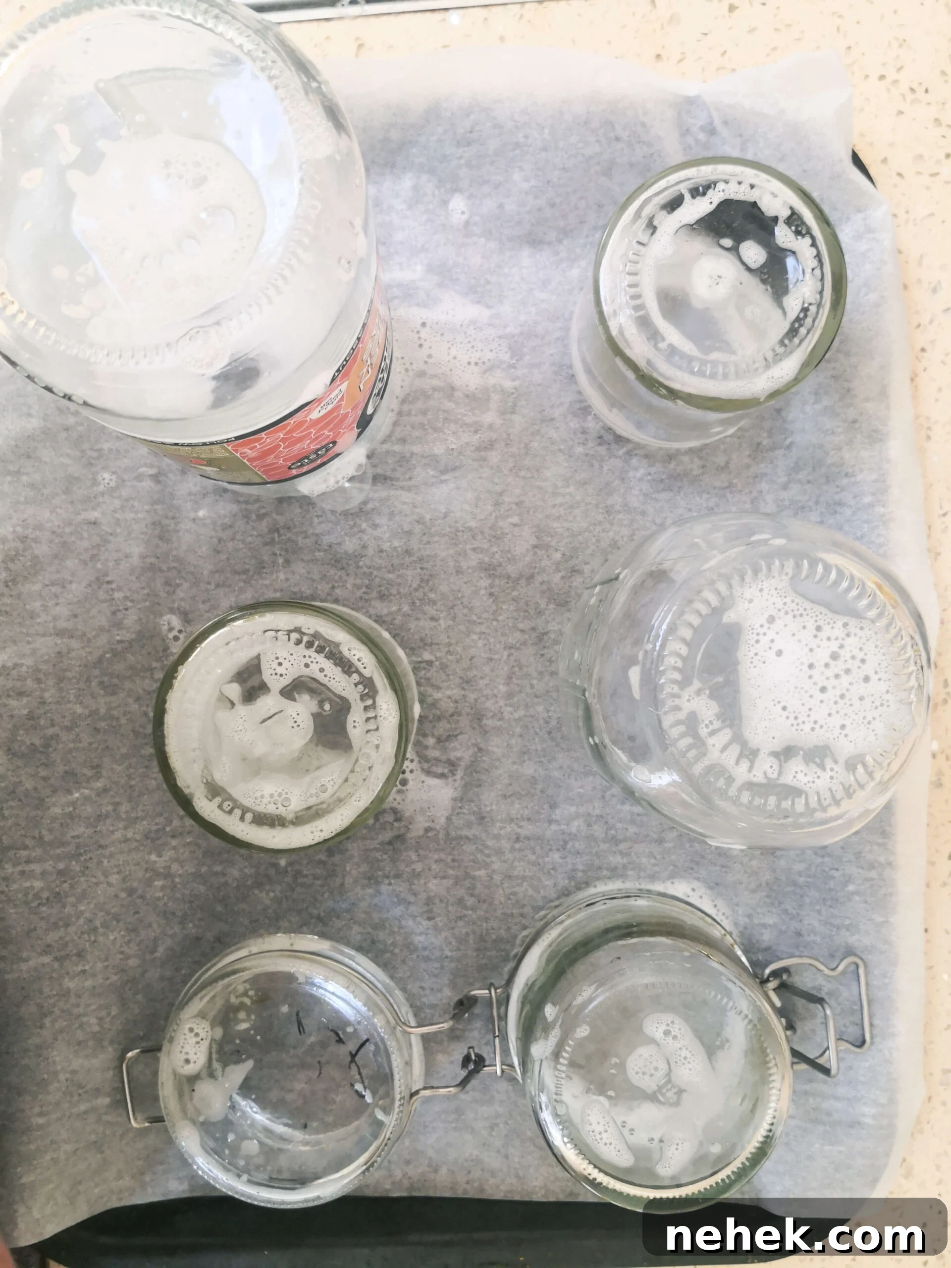 Soapy glass jars standing upright on a lined oven tray.