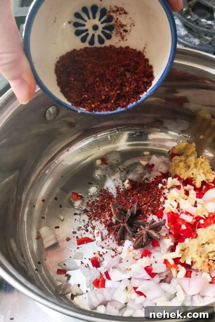 Spices being added to small silver pot with other chilli oil ingredients in a small silver pot.