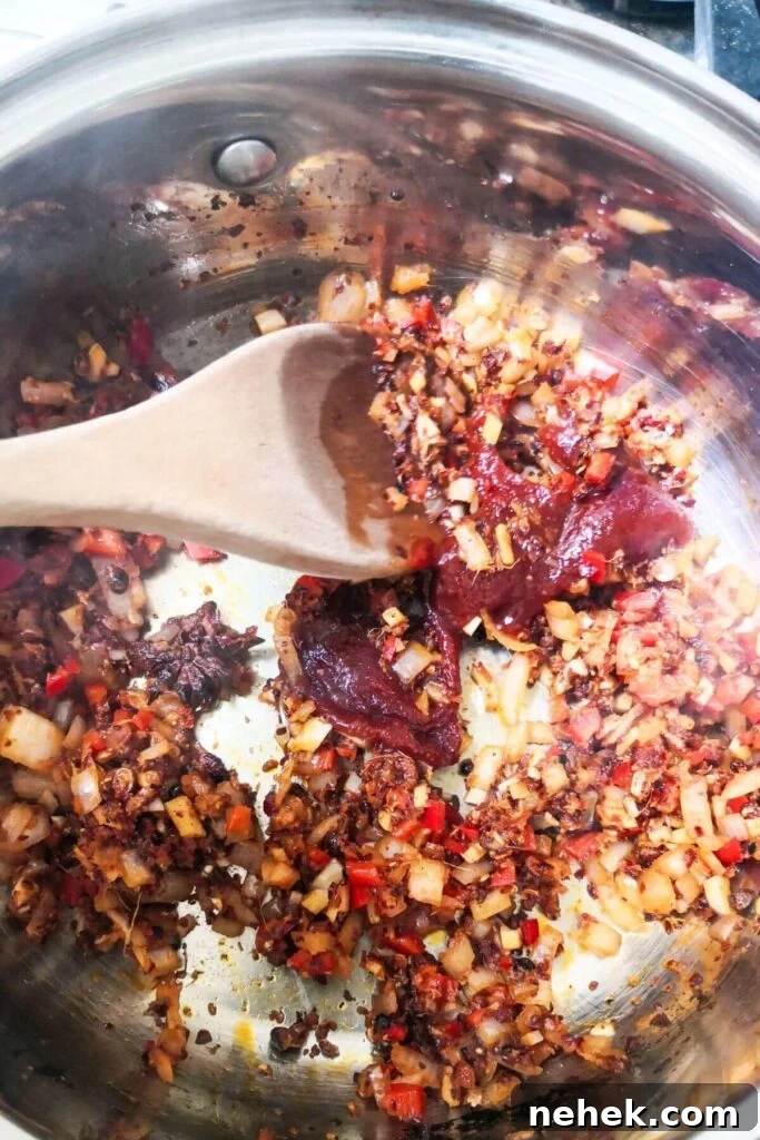 Gochujang paste being stirred into chilli oil ingredients in a small silver pot.