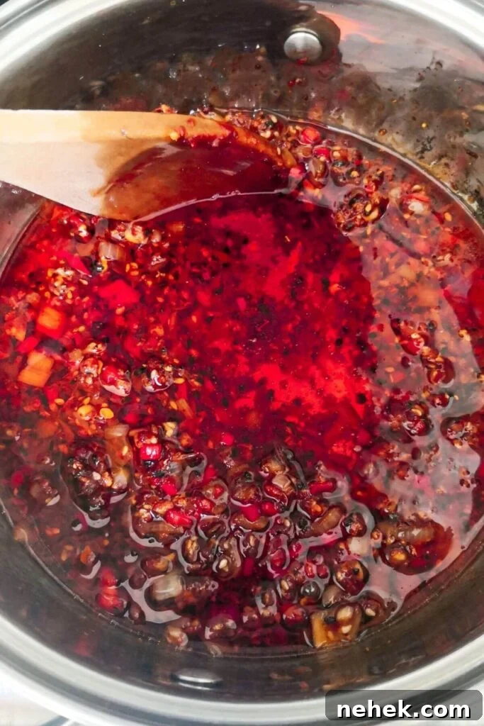 Chilli oil cooking in a small silver pot with a wooden spoon inside.