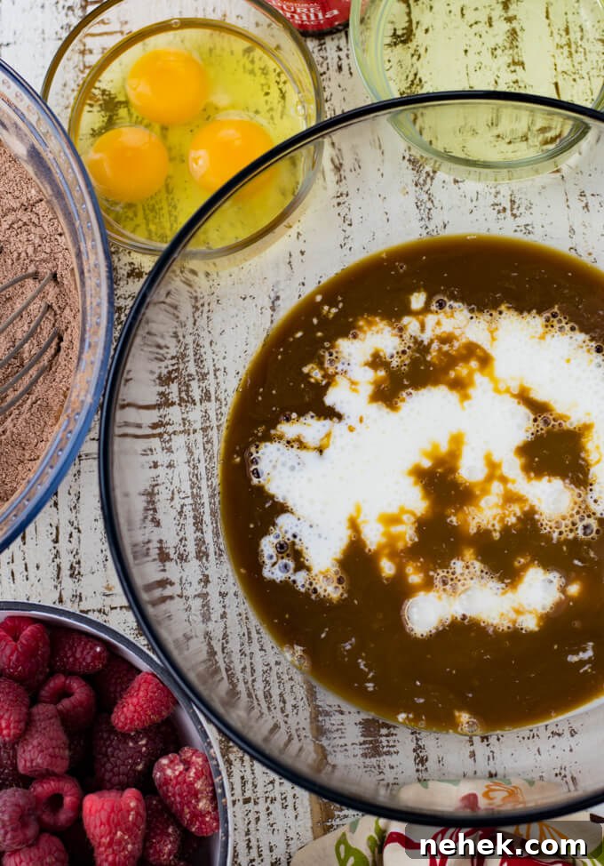 a mixing bowl of coffee and buttermilk for a layered cake. Bowls of eggs, oil, dry ingredients, and fresh raspberries. A colorful napkin sits next to the bowl.