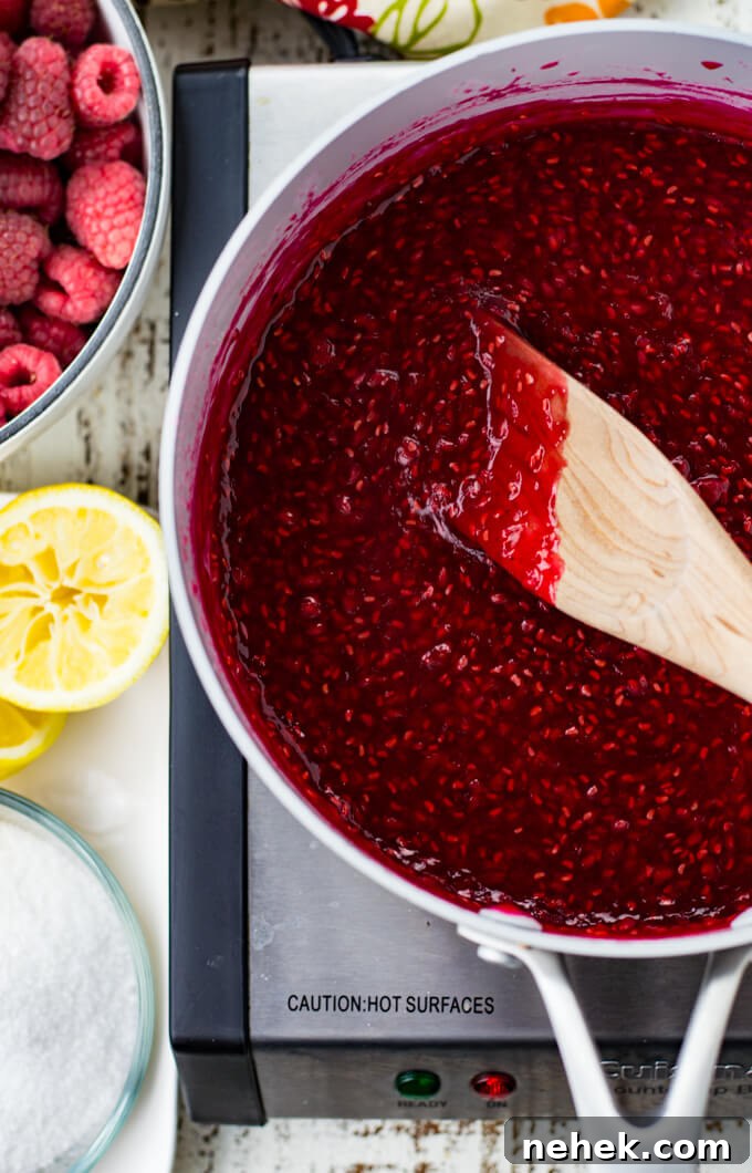 A pan of raspberry filling with a bowl of fresh raspberries, squeezed halved lemons and sugar.