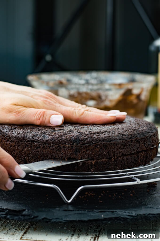 A round chocolate cake being sliced horizontally through the middle with a serrated knife.