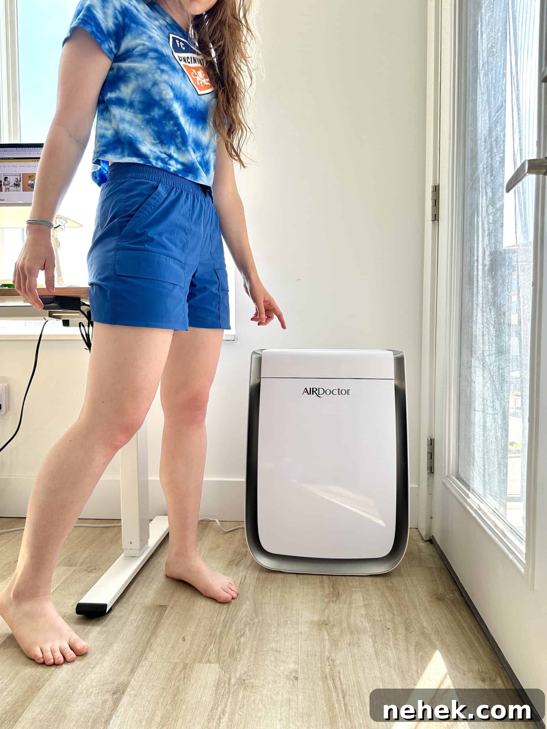 a woman in a blue shirt pointing to the AirDoctor air filter in her home
