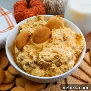 Close up of cream cheese pumpkin dip in a white bowl surrounded by vanilla wafers and graham crackers.