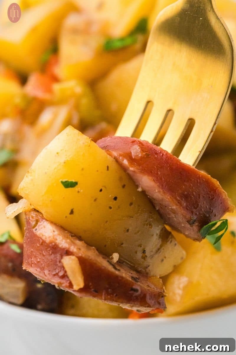 a fork stacked with crockpot sausage & potatoes sprinkled with parsley.