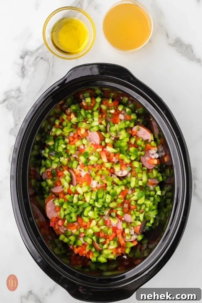 a prep image of a crockpot full of cubed potatoes, sausage, onion, red bell pepper, green bell pepper, and garlic with bowls of broth and oil next to it.