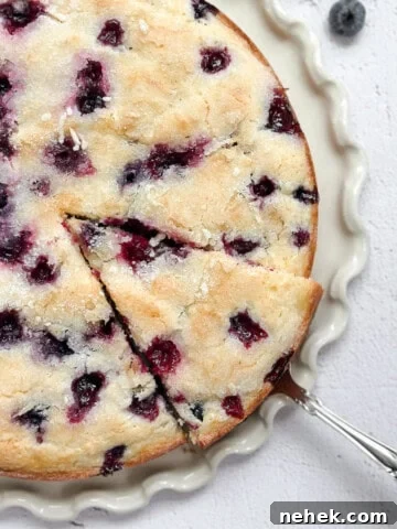 lemon blueberry sour cream cake on a cake plate with a spatula taking a piece.
