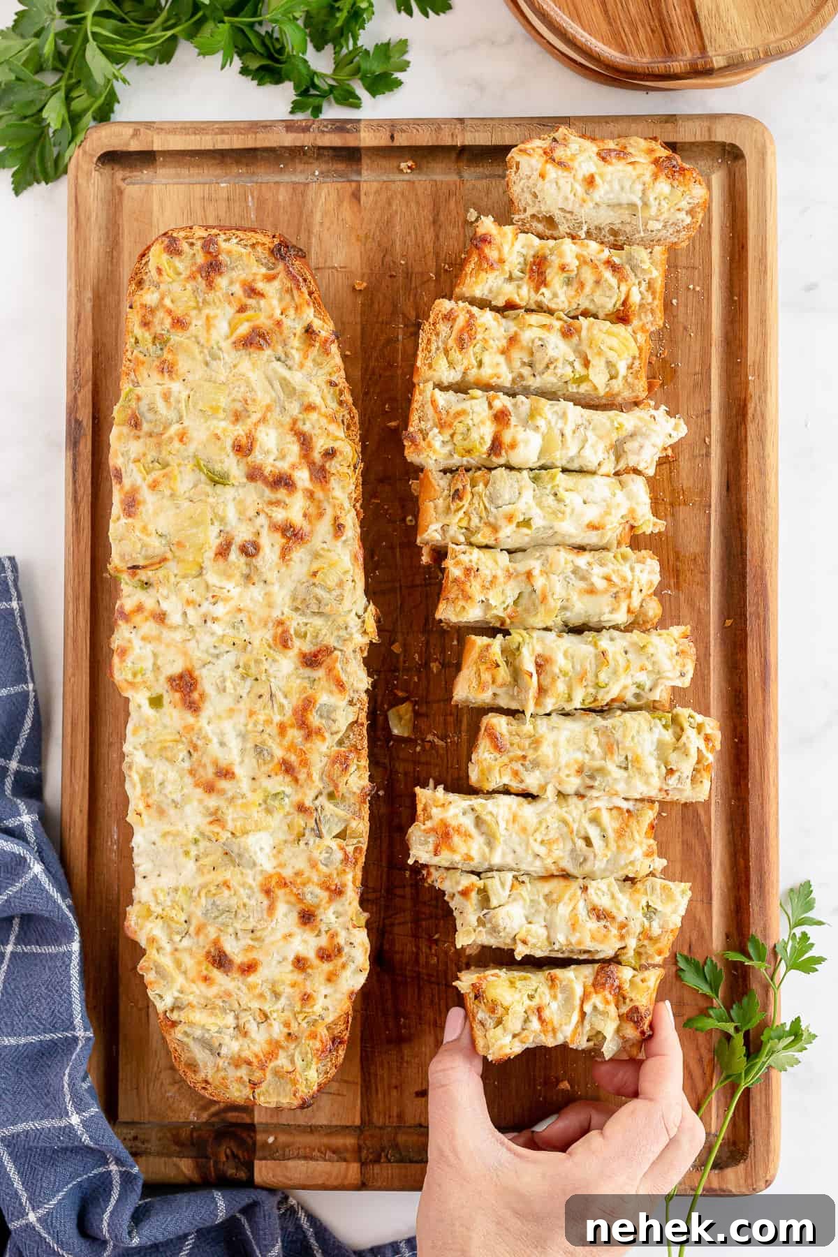 A hand reaching for a slice of Cheesy Artichoke Bread on a cutting board.