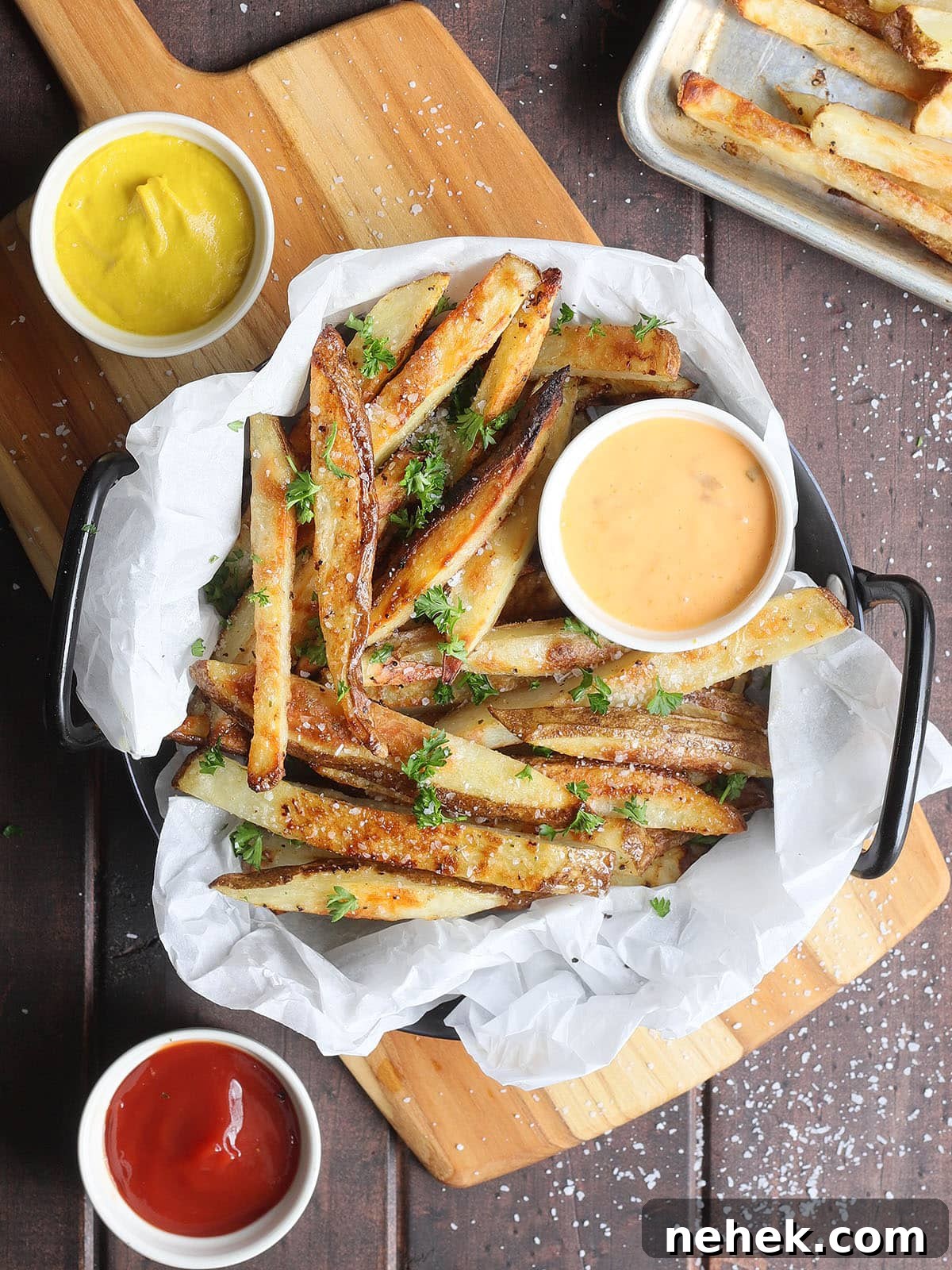 Crispy Oven-Baked French Fries Recipe for Perfect Crunch 2 Oven baked French fries in a parchment paper lined dish garnished with salt and chopped fresh parsley.