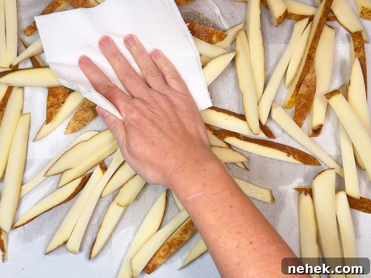 Crispy Oven-Baked French Fries Recipe for Perfect Crunch 5 Hand using a paper towel to blot excess moisture from cut potatoes after they have soaked in water.