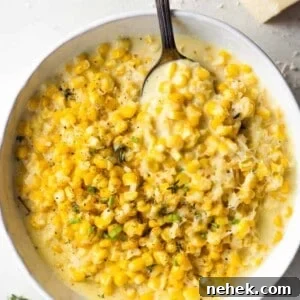 White bowl filled with cream corn, serving spoon, off to the side is a wedge of parmesan cheese.