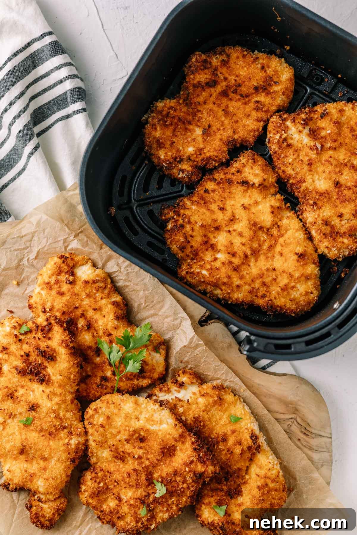 Top-down image crispy, golden chicken cutlets in air fryer basket with some on the table next to it