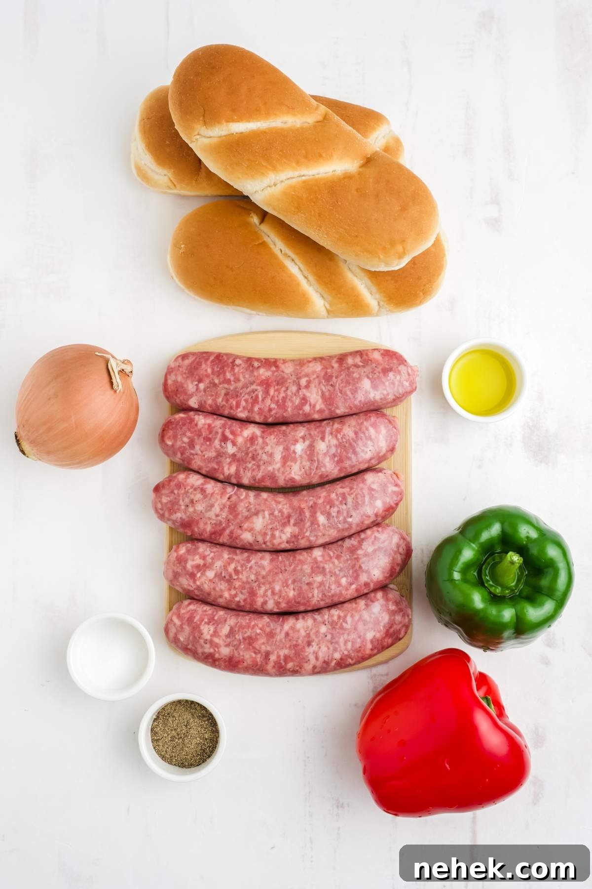 Various ingredients for making air fryer brats with peppers and onions are arranged on a white surface, including uncooked sausages, sandwich rolls, an onion, bell peppers, oil, salt, and pepper.