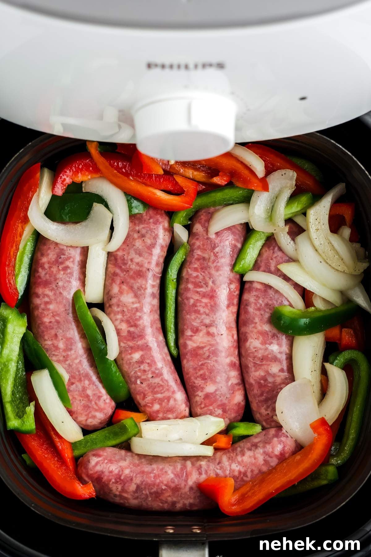 Raw air fryer Johnsonville smoked brats with peppers and onions are placed in an air fryer basket alongside sliced green and red bell peppers. An air fryer lid is partially visible at the top.