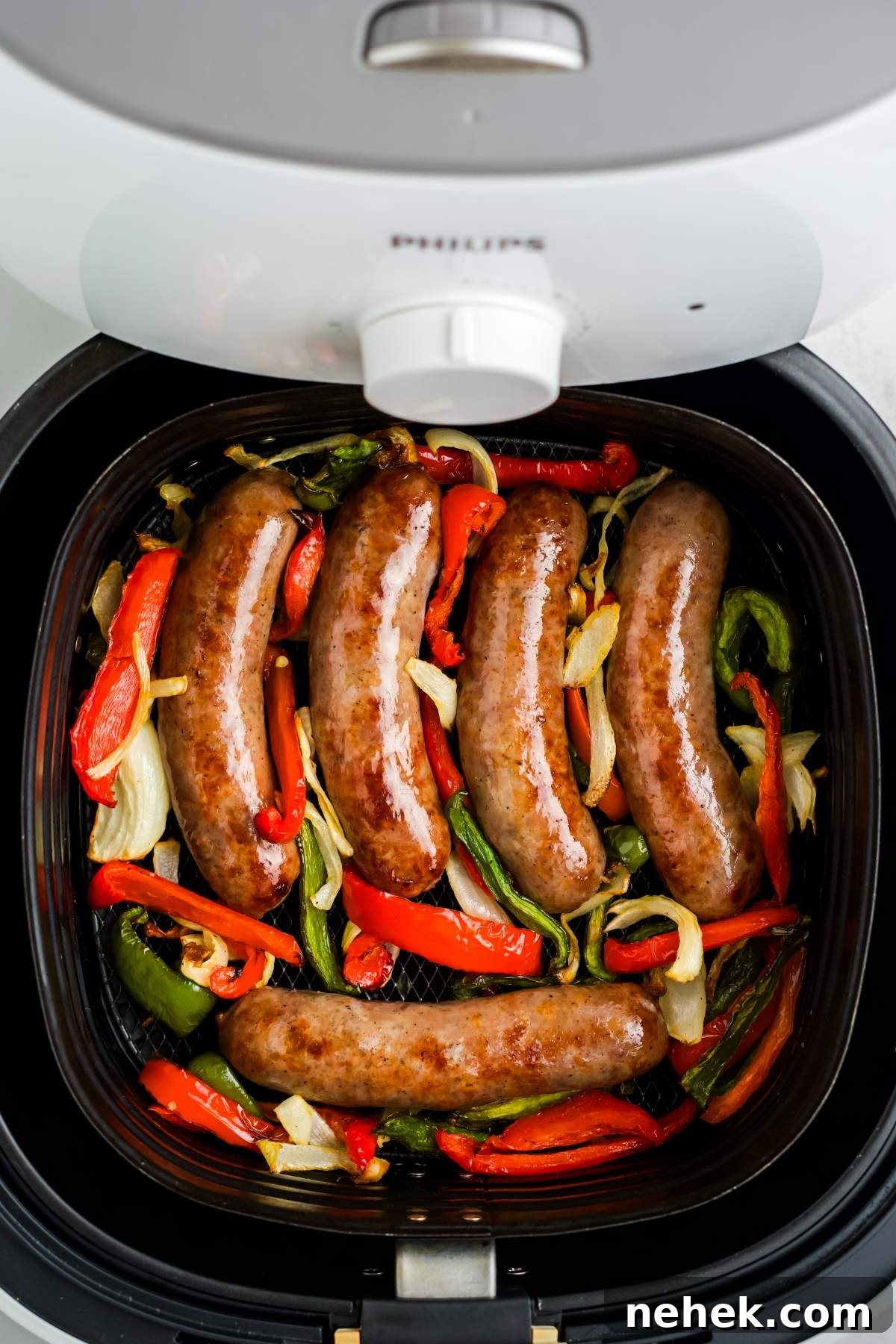 Air fryer brats with peppers and onions are cooking together in an air fryer.