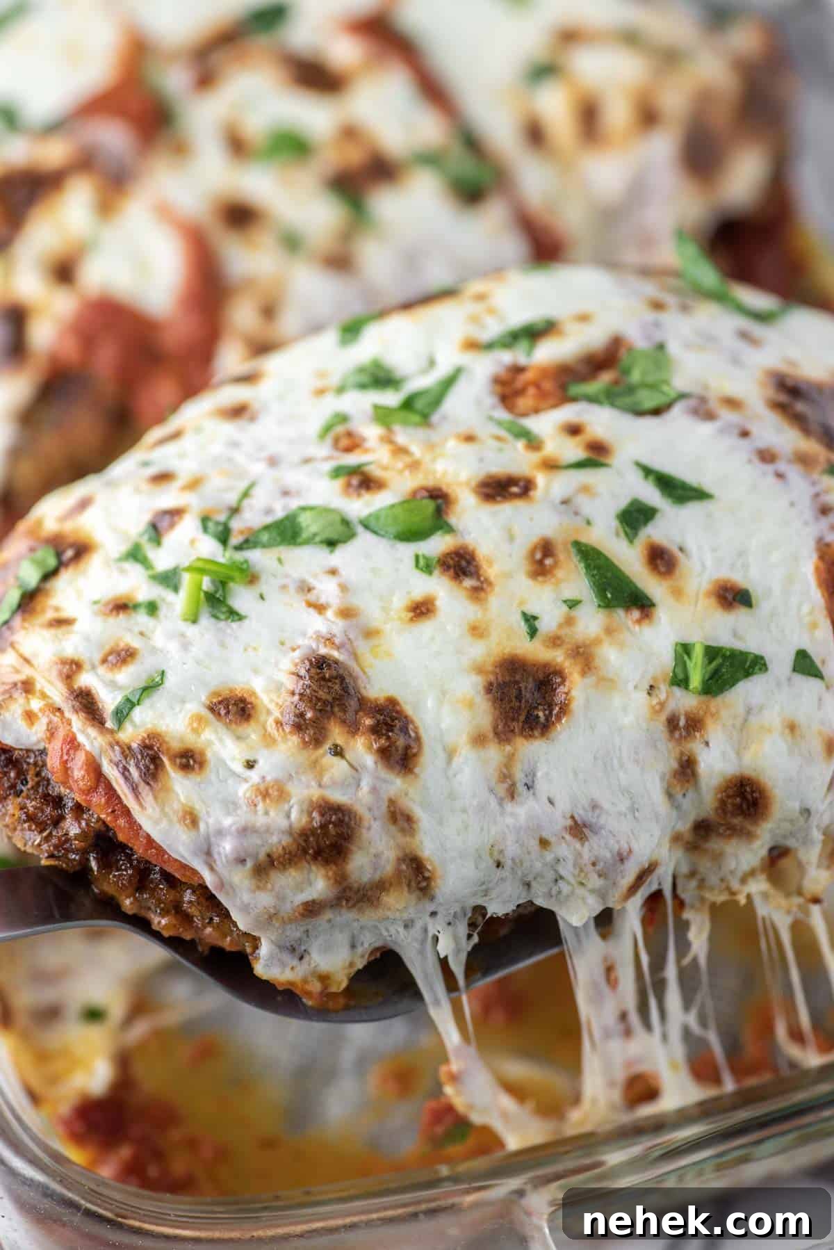 Breaded chicken parmesan being lifted out of glass dish.