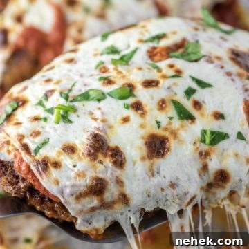 Breaded chicken parmesan being lifted out of glass dish.