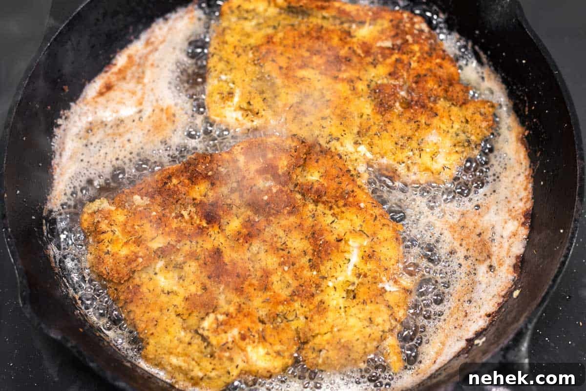 Chicken being cooked in skillet with oil.