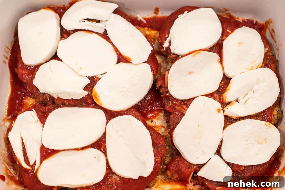 Chicken in baking dish with marinara sauce and cheese.