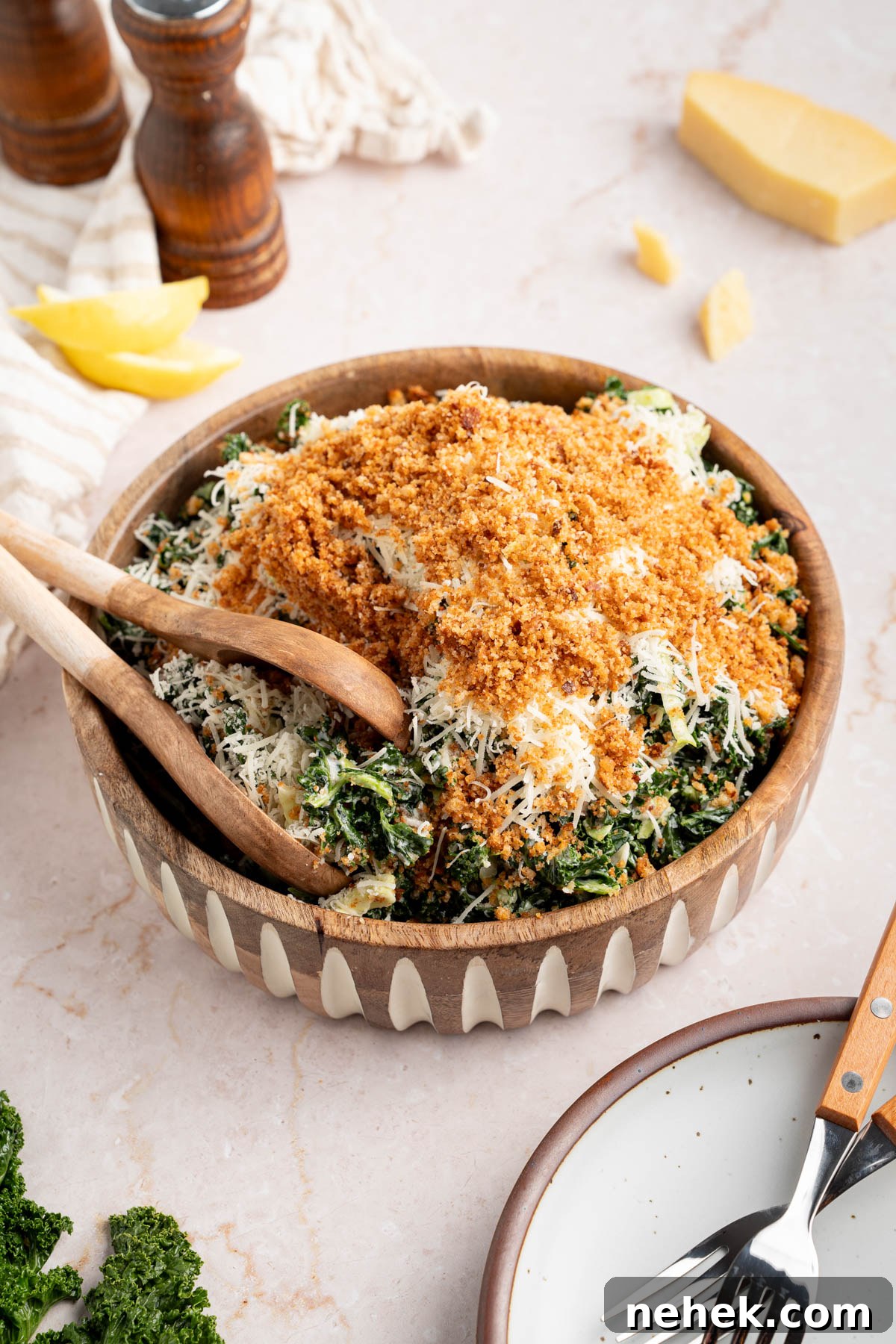A kale caesar salad piled high in a large serving bowl with serving tongs on the side.