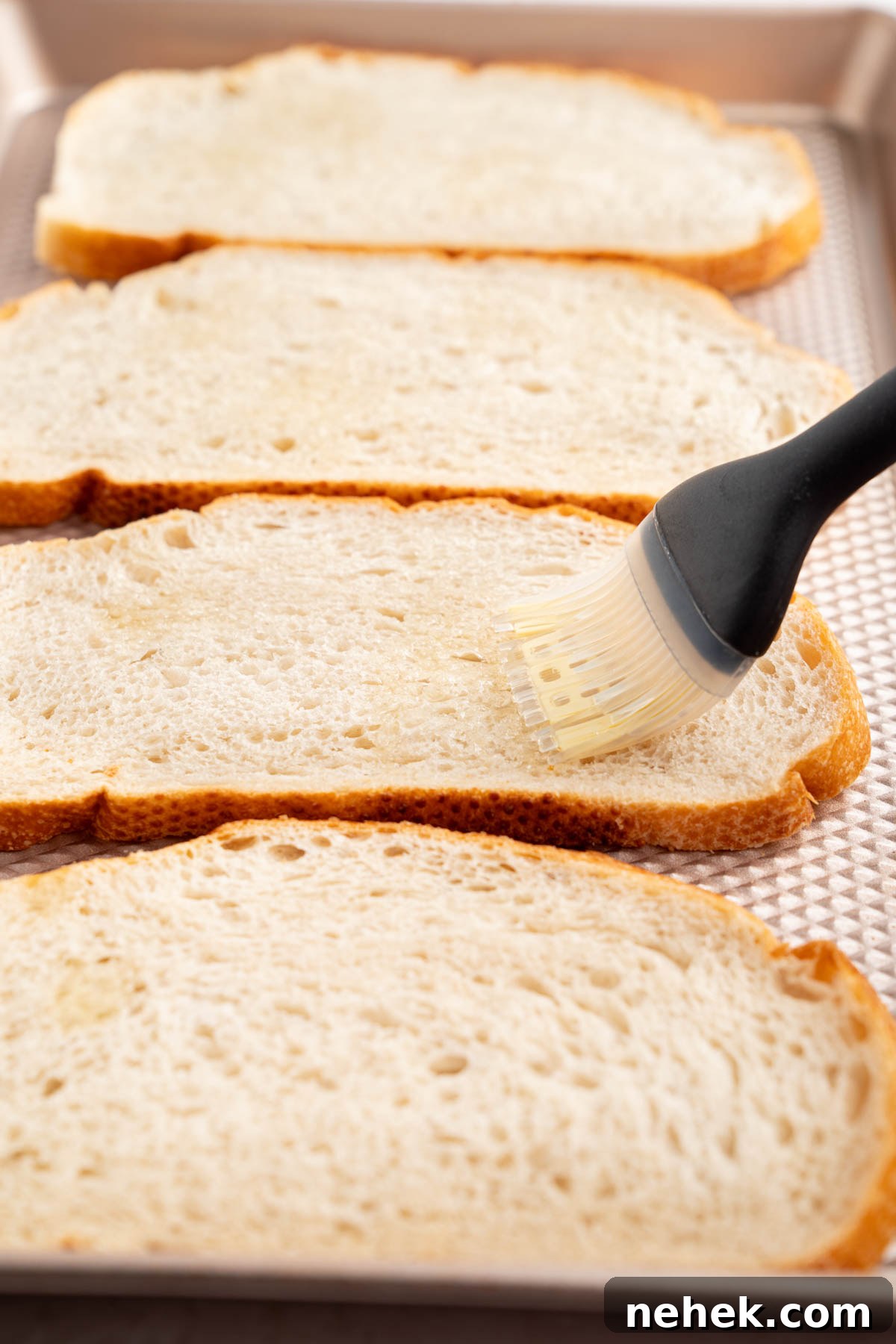 A pastry brush brushes olive oil on the bread slices before baking.