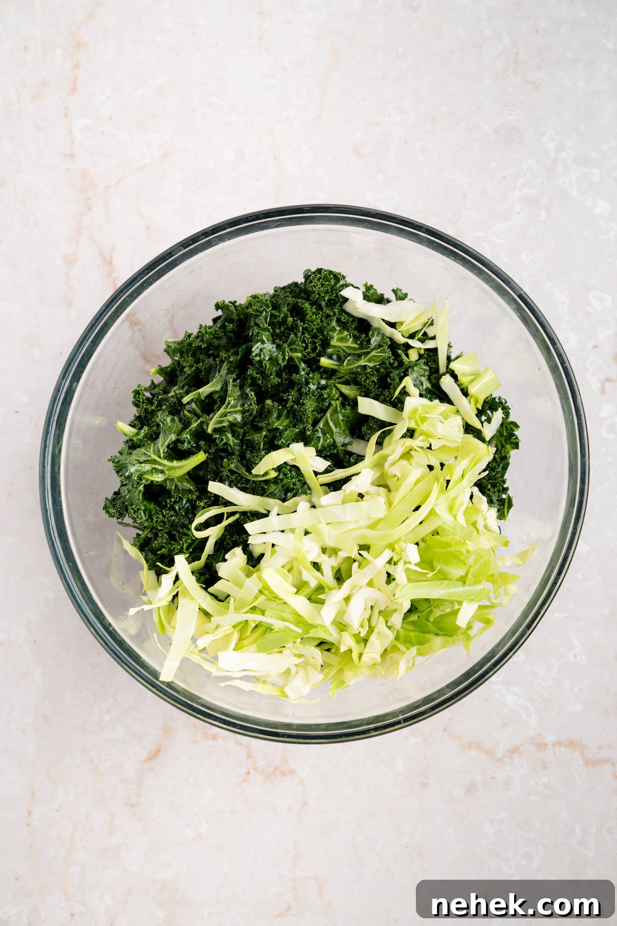The shredded cabbage in the bowl with the massaged kale.