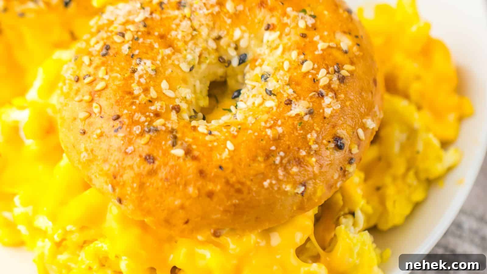 15 Delicious Easter Recipes to Make Your Celebration Shine 4 A sesame seed bagel sits on top of a serving of scrambled eggs with melted cheese on a white plate.