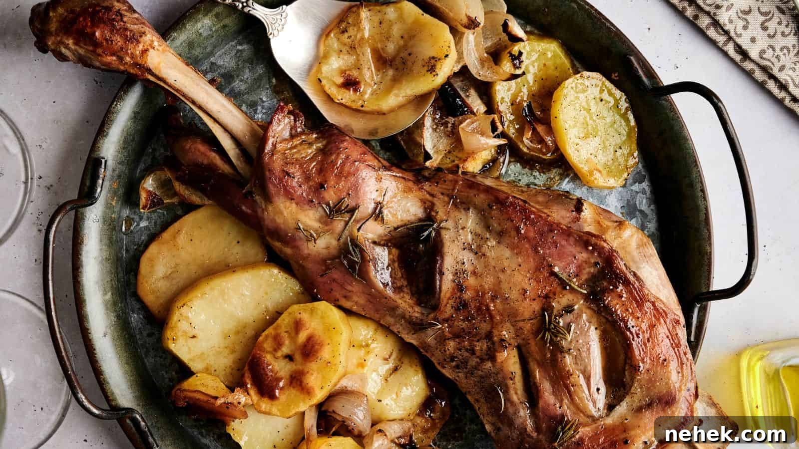 Roasted lamb leg on a platter with sliced potatoes, lemon, and herbs. A knife is placed beside the dish.