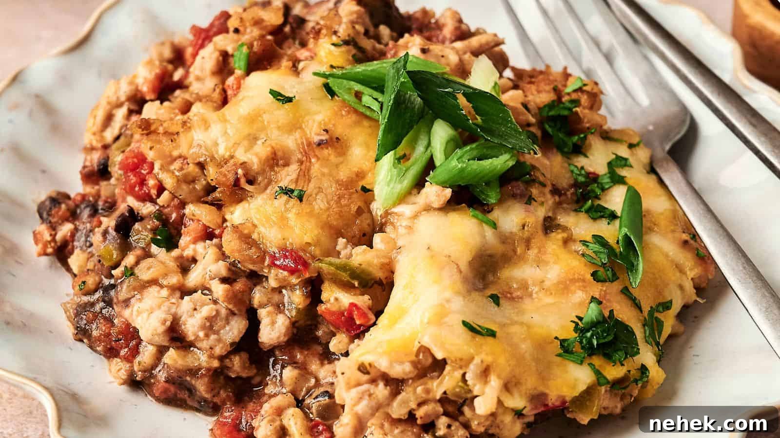A plated serving of cheesy casserole with ground meat, topped with sliced green onions and parsley, accompanied by a fork.