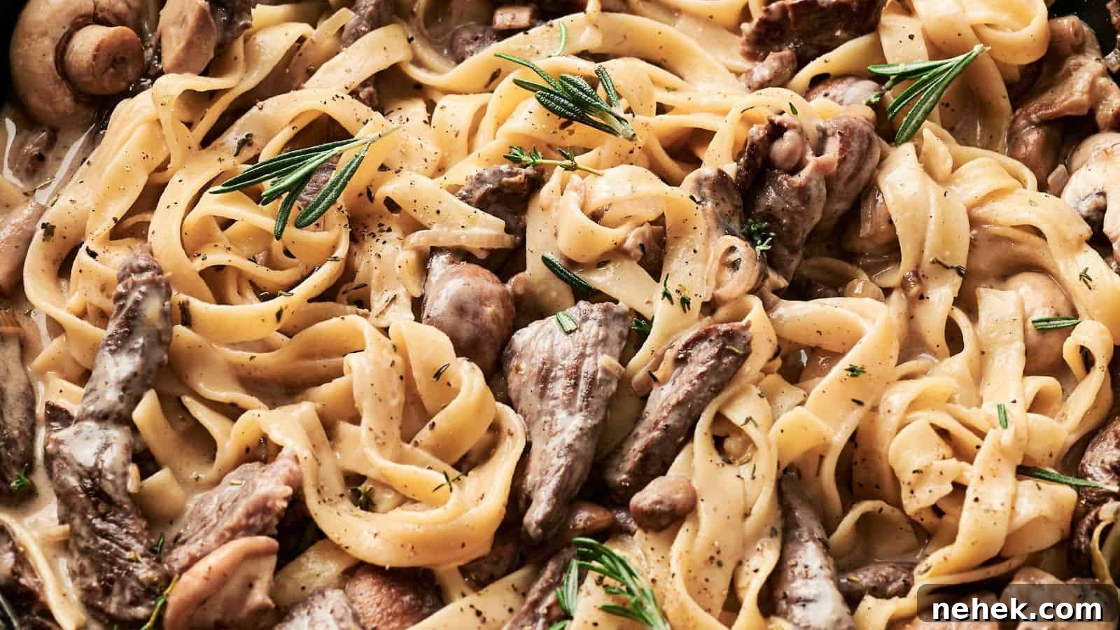 A close-up of fettuccine pasta with creamy sauce, reminiscent of Beef Stroganoff, paired with sliced beef, mushrooms, and sprigs of rosemary.