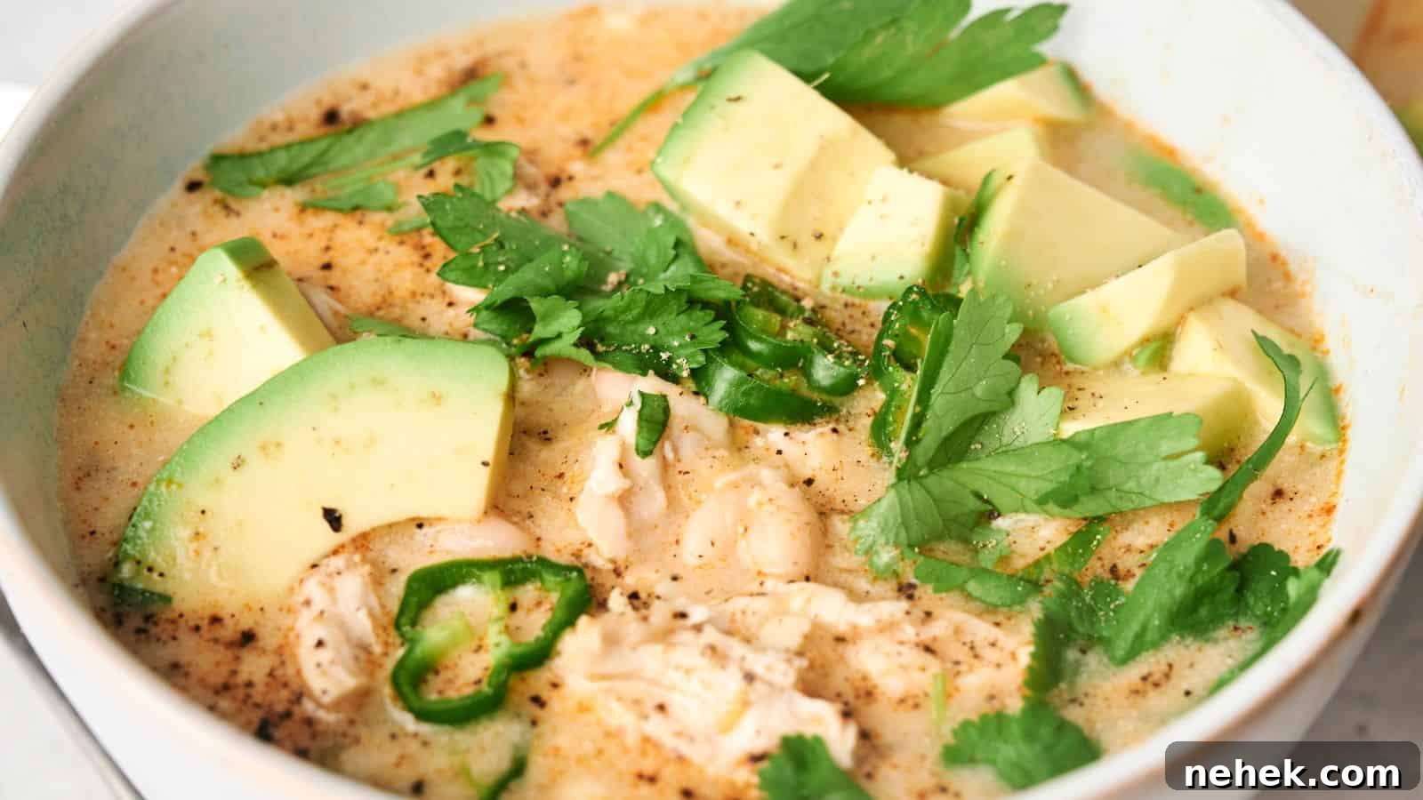 A bowl of creamy White Chicken Chili with chunks of chicken, sliced avocado, green jalapeño peppers, white beans, and fresh cilantro.