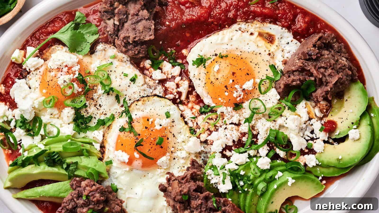 A plate of huevos rancheros with sunny-side-up eggs, avocado slices, refried beans, tomato sauce, crumbled cheese, and garnished with green onions and cilantro.