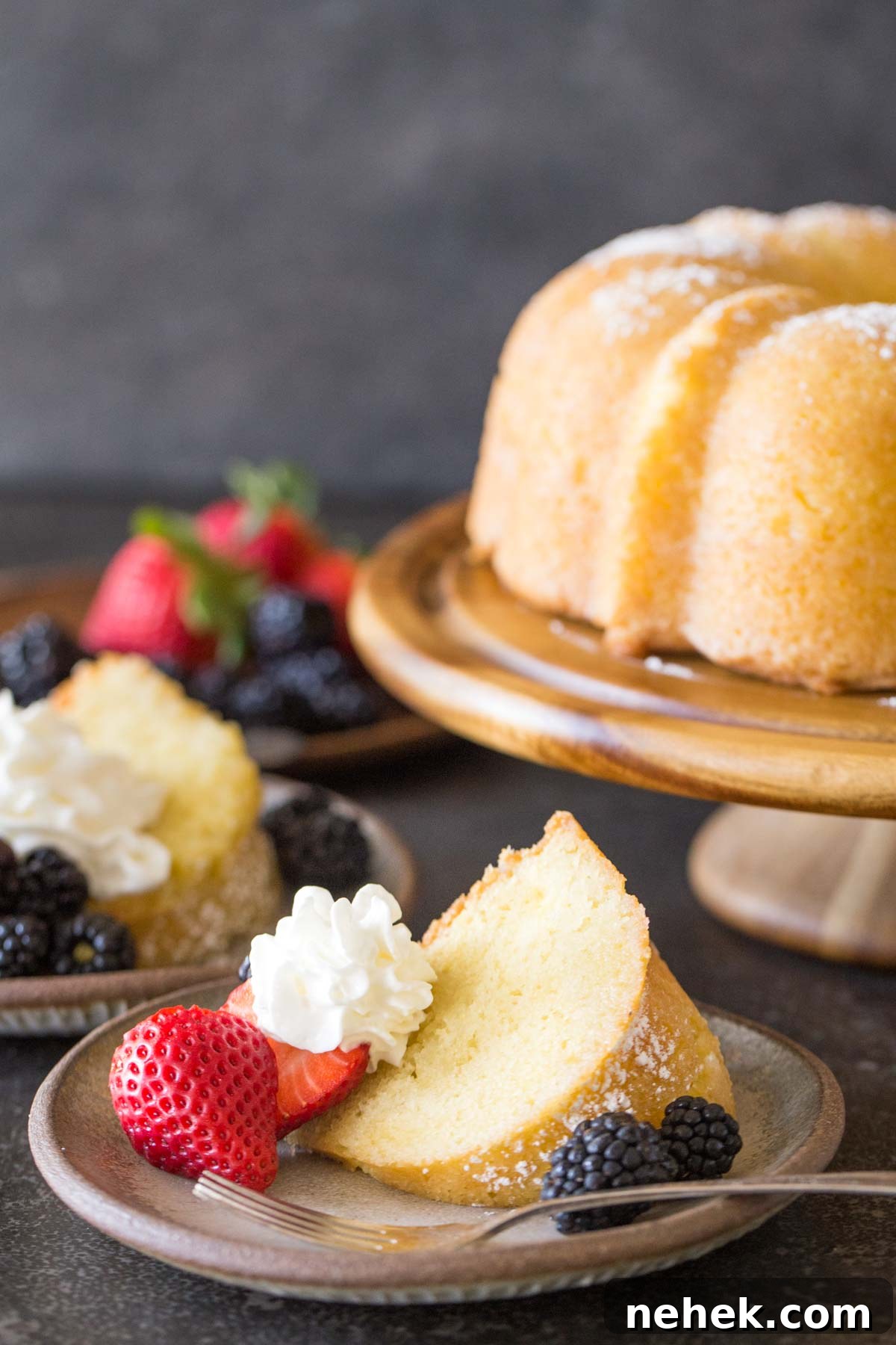 Classic Kentucky Butter Cake Recipe: Moist Southern Pound Cake 3 Kentucky Butter Cake on wooden cake stand with whipped cream and berries on a grey background.