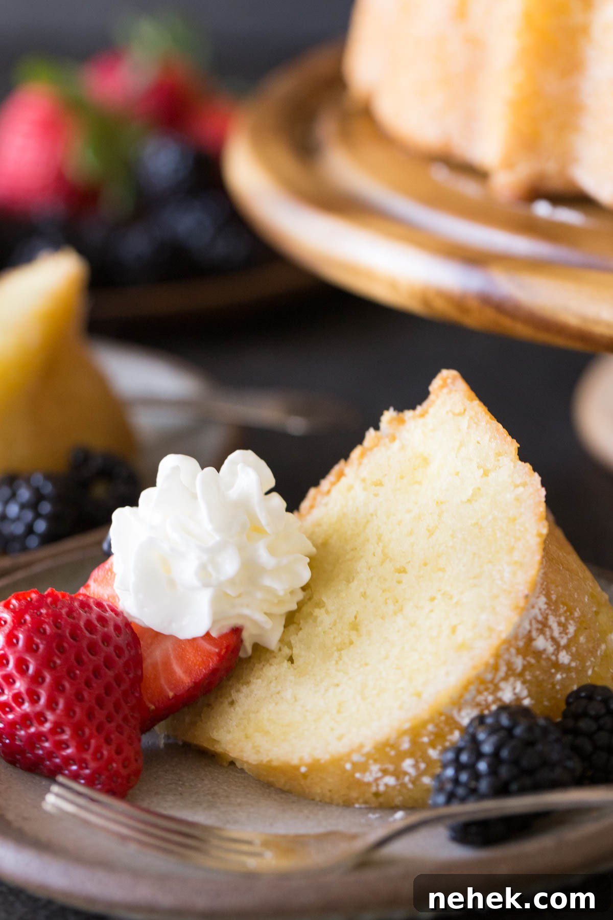 Classic Kentucky Butter Cake Recipe: Moist Southern Pound Cake 5 Kentucky Butter Cake on wooden cake stand with whipped cream and berries on a grey background.