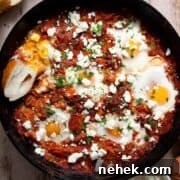Healthy shakshuka with poached eggs, tomato sauce, and feta cheese served in a cast iron pan