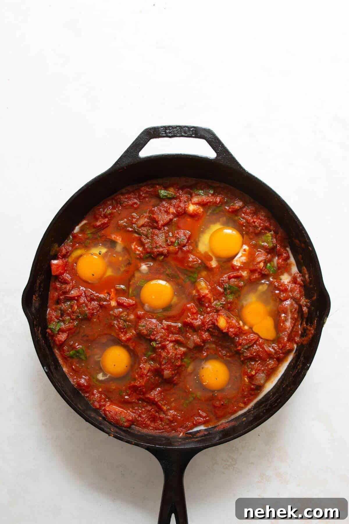 Cracking eggs into wells in the tomato sauce for shakshuka