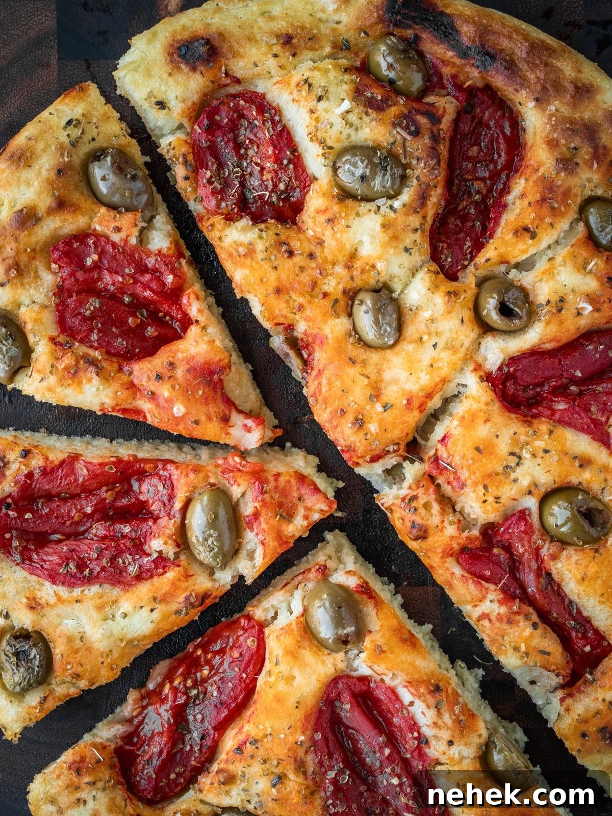 Focaccia Barese slices garnished with tomatoes, green olives and oregano on a wooden board.