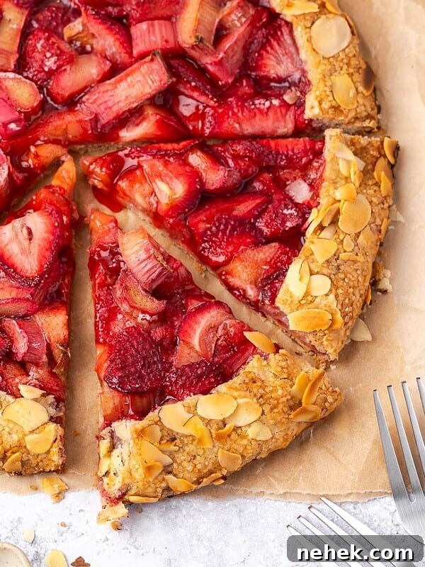 Sliced strawberry rhubarb galette with almond crust on parchment paper.
