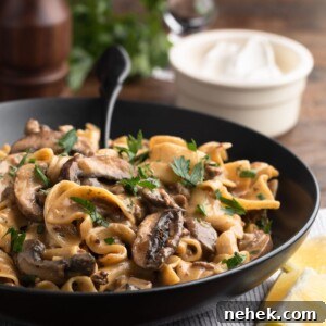 ground beef stroganoff in a black ceramic bowl with a black fork, in front of a bowl of sour cream, a glass of red wine, and a pepper mill