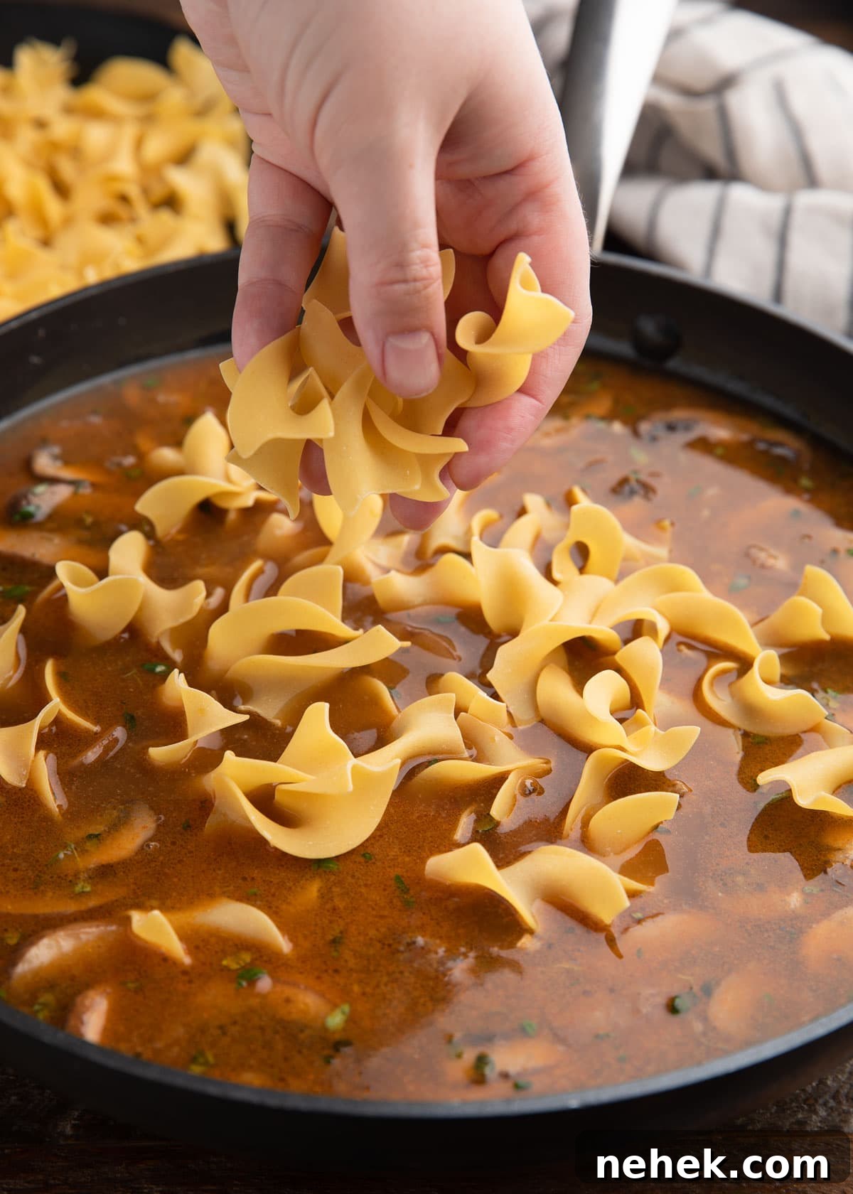 adding extra wide egg noodles to beef broth in a skillet