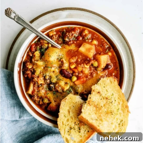 A bowl of shepherd's pie chili topped with herbs, served with a spoon and two slices of toasted bread on the side.