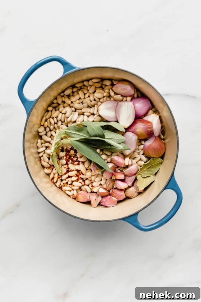A blue pot filled with white beans, sage, shallots, garlic and bay leaves