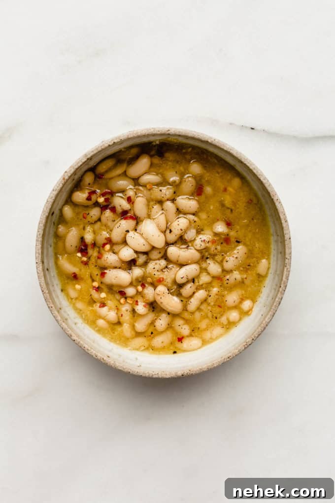 a bowl of white beans in broth topped with chili flakes