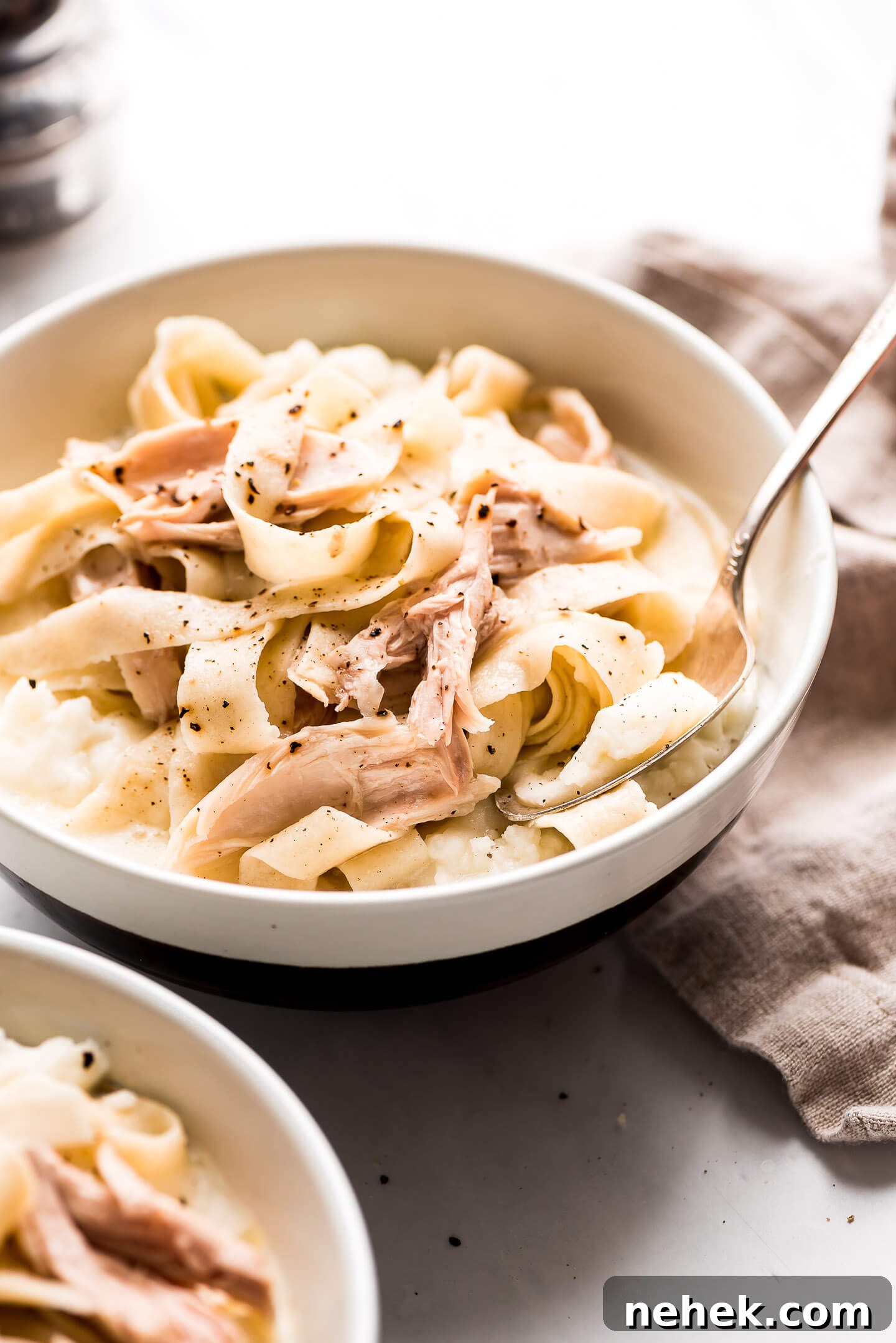 Creamy Chicken and Noodles Served Over Garlic Mashed Potatoes 3 A bowl of Chicken and Noodles over mashed potatoes, garnished with fresh cracked pepper.