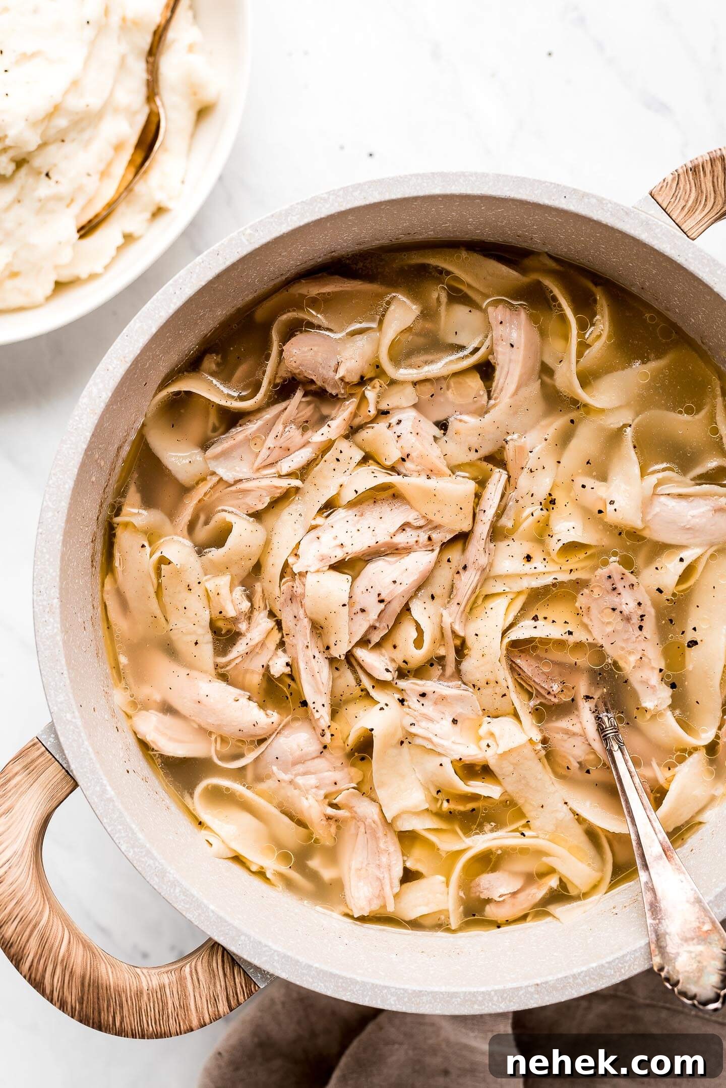 Creamy Chicken and Noodles Served Over Garlic Mashed Potatoes 4 A large pot of shredded chicken and homemade egg noodles and a bowl of mashed potatoes to the side.