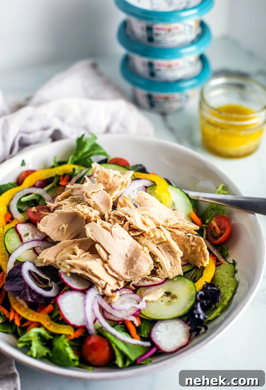 Vertical side shot of colorful salad topped with big flakes of tuna. Product packaging is in the background.