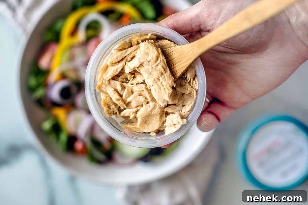 Close up shot of opened package of tuna, salad in the background.
